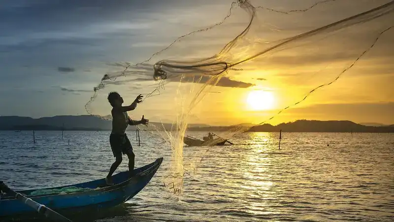 A fisherman casting his net at sunset off Daman